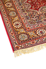 Acercamiento lateral de alfombra oriental con fondo rojo, diseño floral minucioso y borde decorativo en tonos beige, azul suave y dorado