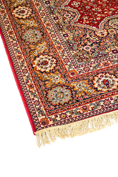 Acercamiento lateral de alfombra oriental con fondo rojo, diseño floral minucioso y borde decorativo en tonos beige, azul suave y dorado