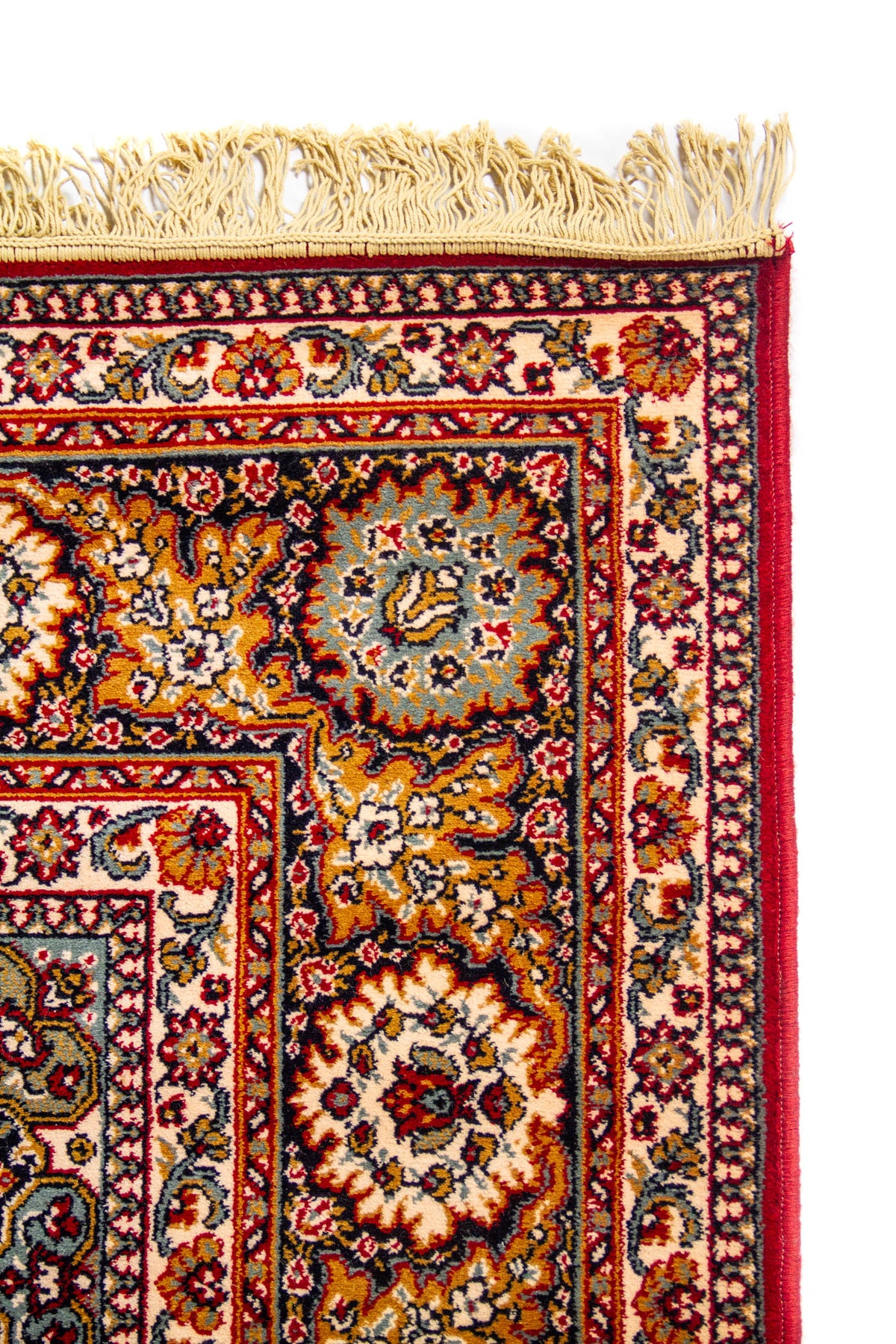 Primer plano de la esquina de una alfombra clásica con flecos claros, borde rojo y guarda floral ornamentada en tonos beige y azul.