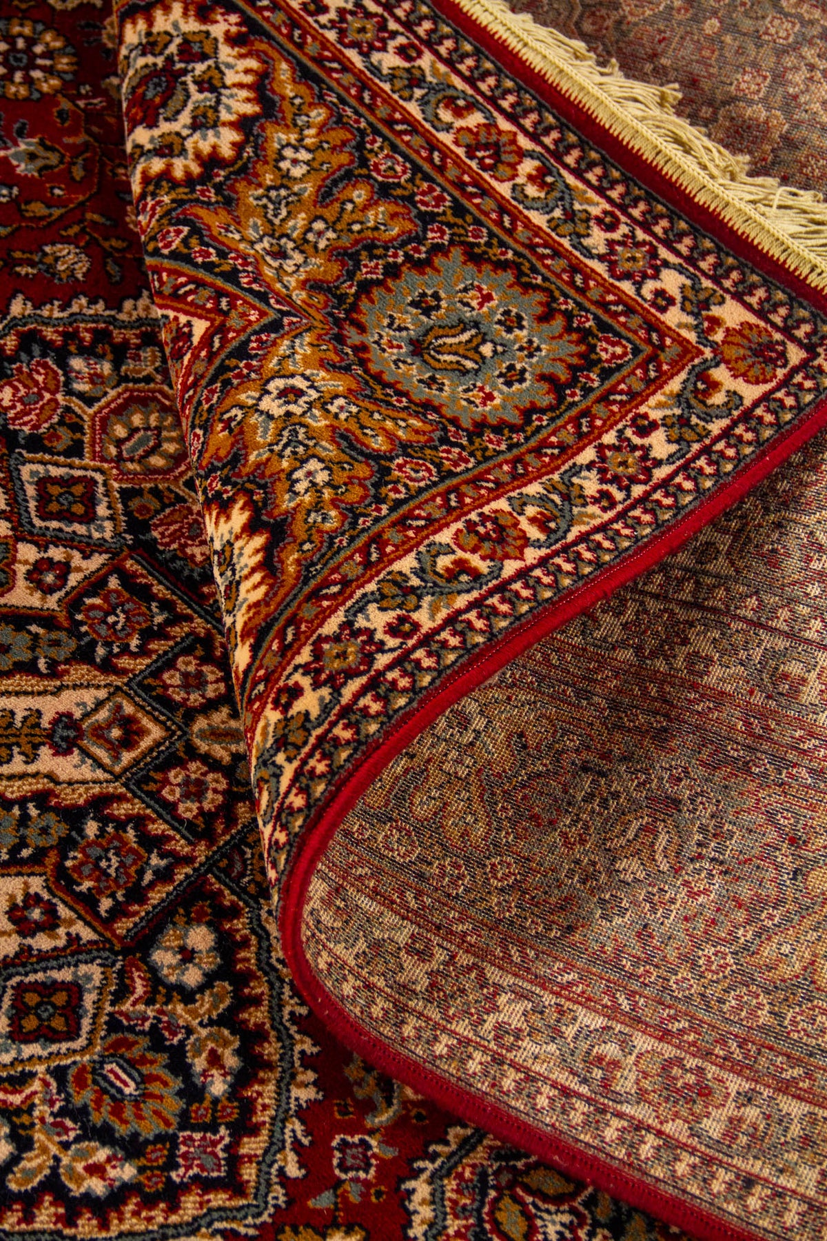 Detalle de alfombra oriental parcialmente doblada que deja ver el reverso, la textura del tejido y la riqueza del diseño geométrico y floral del borde.
