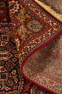 Detalle de alfombra oriental parcialmente doblada que deja ver el reverso, la textura del tejido y la riqueza del diseño geométrico y floral del borde.