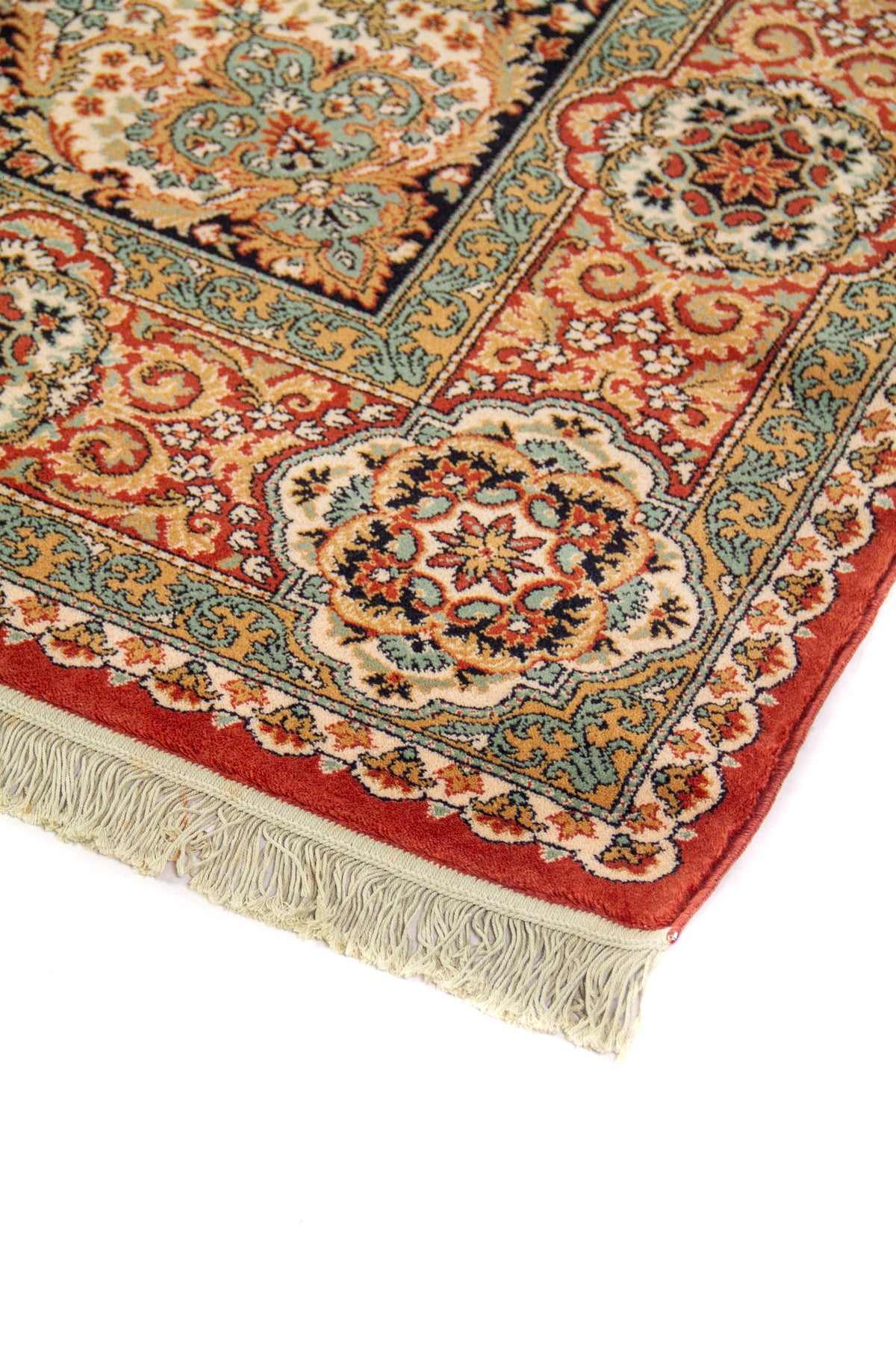 Detalle de esquina de alfombra oriental con guarda floral en tonos rojo, beige y celeste, acabado aterciopelado y flecos color blanco suave.