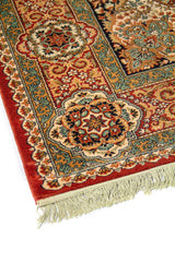 Acercamiento del borde de alfombra clásica con motivos florales simétricos, líneas ornamentales y combinación de rojo, beige, celeste y azul oscuro.