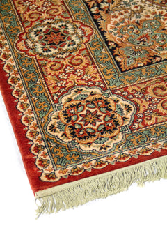 Acercamiento del borde de alfombra clásica con motivos florales simétricos, líneas ornamentales y combinación de rojo, beige, celeste y azul oscuro.