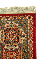 Primer plano de la esquina superior de alfombra tradicional con diseño floral detallado, borde rojo intenso y flecos color blanco suave.
