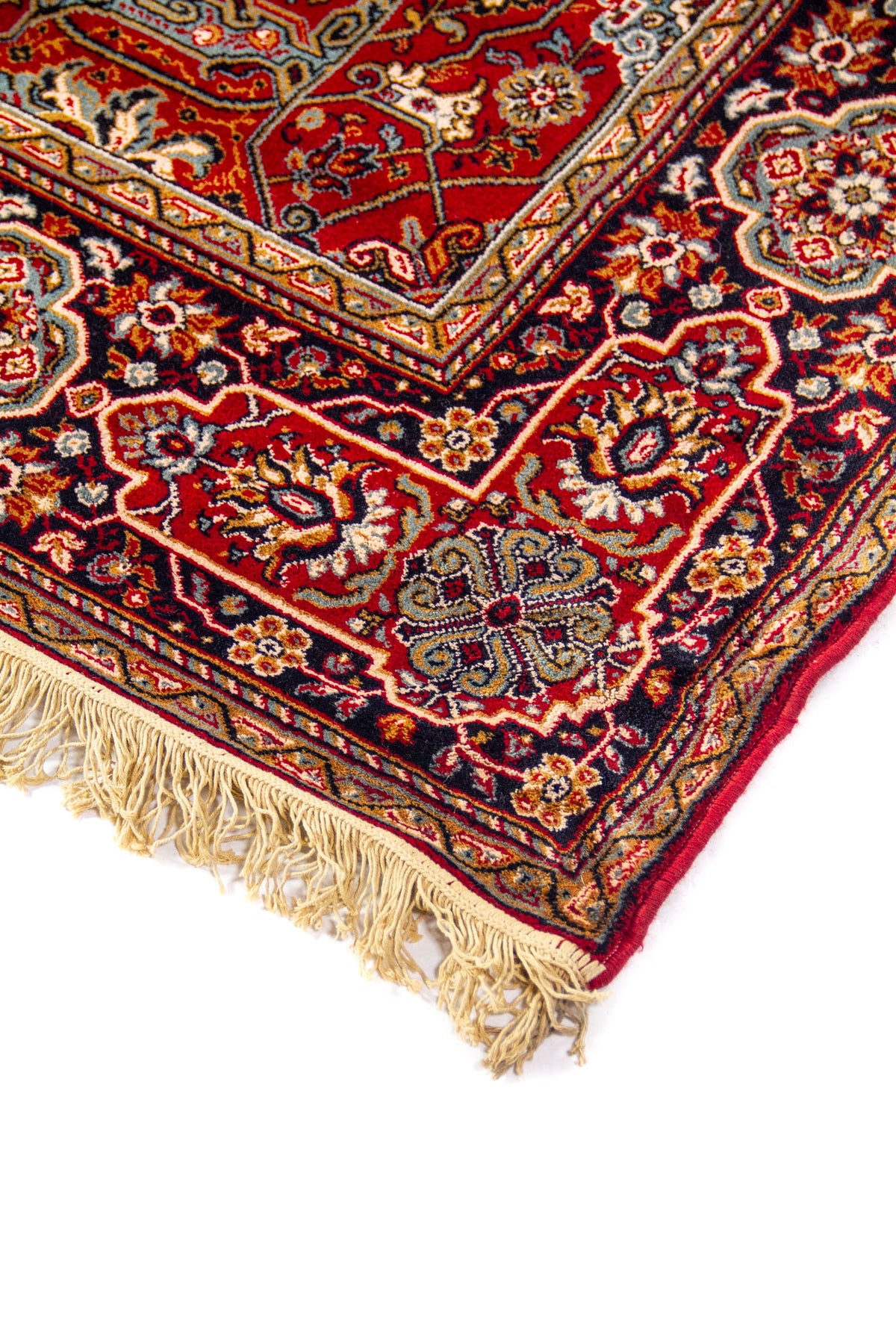 Acercamiento lateral de alfombra oriental con fondo rojo, diseño geométrico detallado y cenefa decorativa en tonos beige, azul oscuro y anaranjado oscuro.