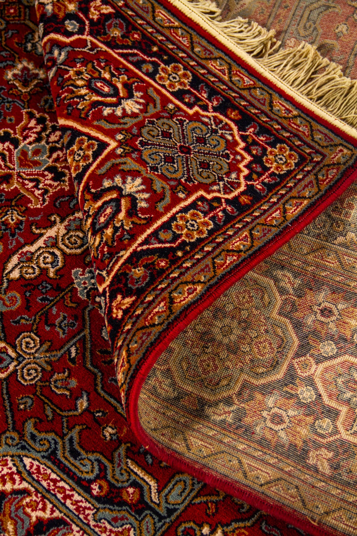 Detalle de alfombra oriental parcialmente doblada que deja ver el reverso, la textura del tejido y la riqueza decorativa del borde.