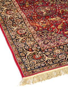 Detalle lateral de alfombra de estilo persa con fondo rojo intenso, borde azul oscuro y motivos florales