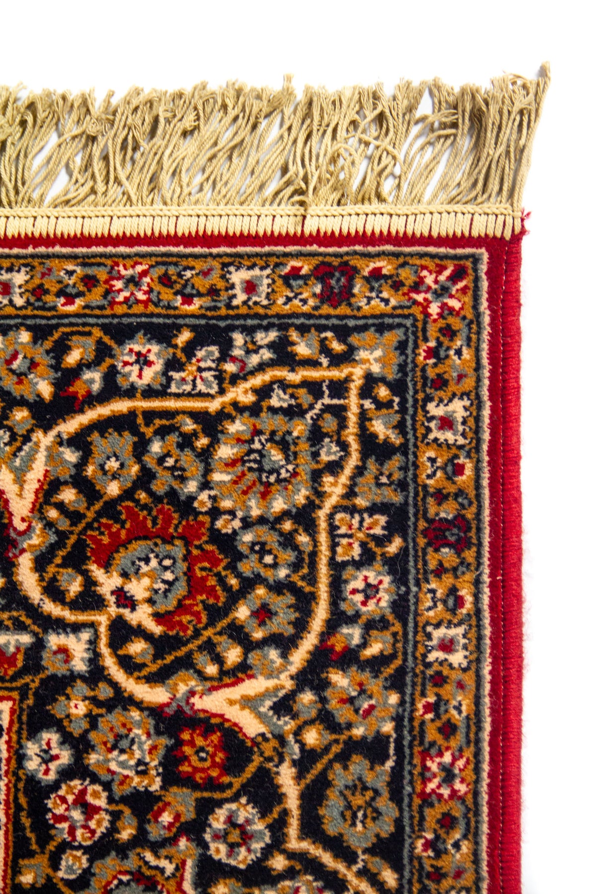 Primer plano de esquina superior de alfombra oriental con flecos beige, ribete rojo y cenefa decorativa.