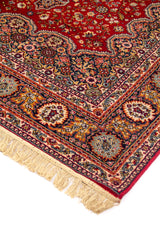 Detalle de esquina de alfombra roja con borde decorativo en tonos beige, azul y dorado, y flecos claros