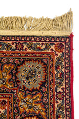 Detalle de esquina superior de alfombra oriental con flecos beige y guarda decorativa en tonos rojo, azul y beige.