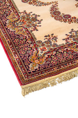 Primer plano del borde de alfombra oriental con fondo beige, motivos florales curvos y terminación con flecos
