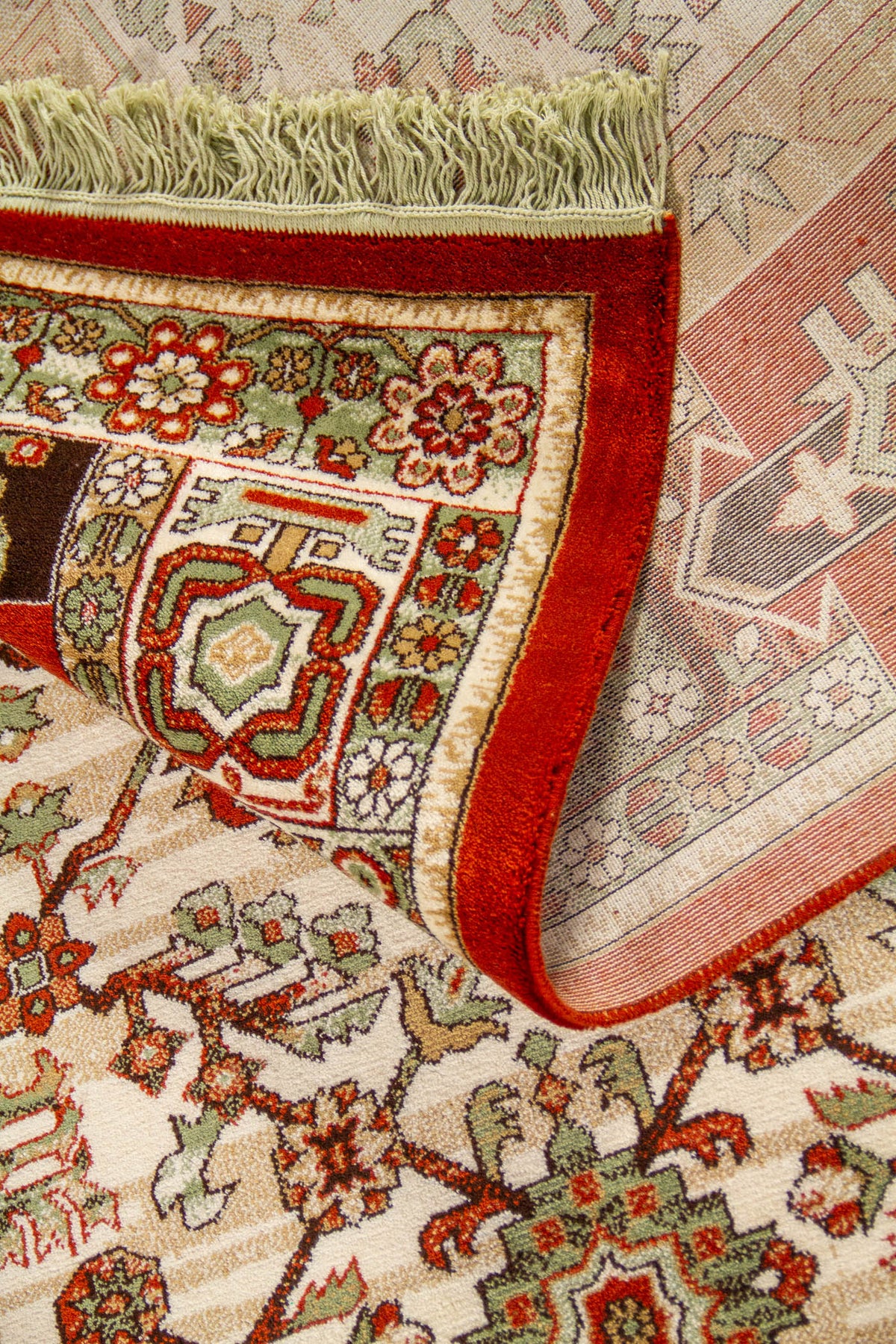 Detalle de alfombra doblada mostrando la textura, el reverso del tejido y el diseño geométrico del borde en tonos rojo y verde