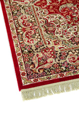 Detalle de esquina de alfombra roja estilo oriental con guarda floral en tonos beige, negro, verde suave y flecos color blanco suave.
