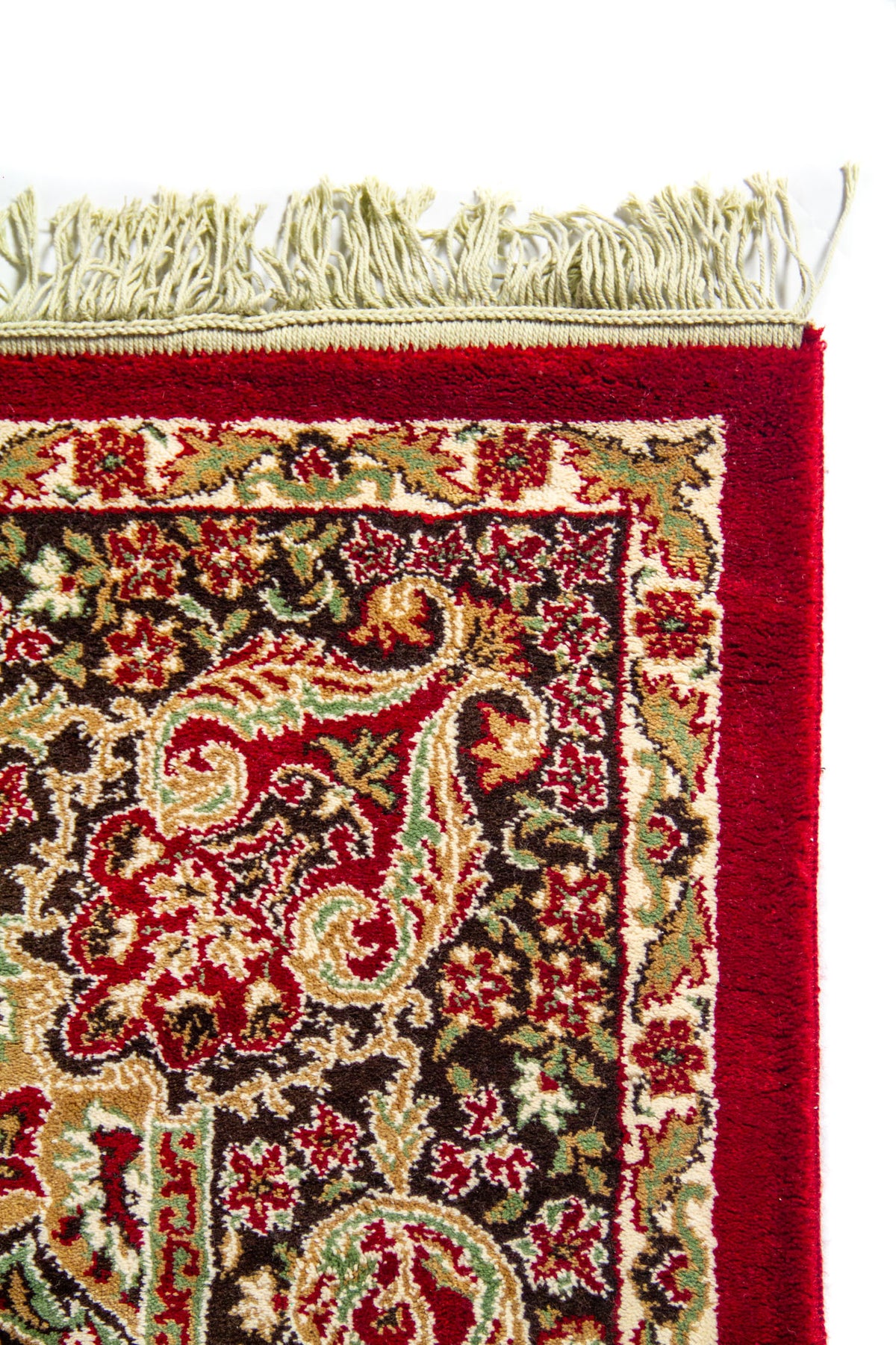 Detalle superior de alfombra oriental roja con flecos blanco suave, borde ancho rojo y guarda floral de inspiración clásica.