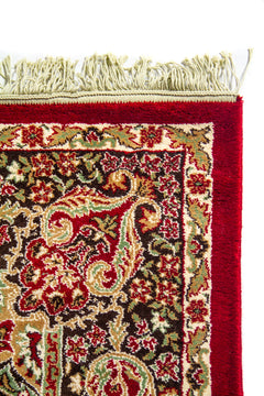 Detalle superior de alfombra oriental roja con flecos blanco suave, borde ancho rojo y guarda floral de inspiración clásica.