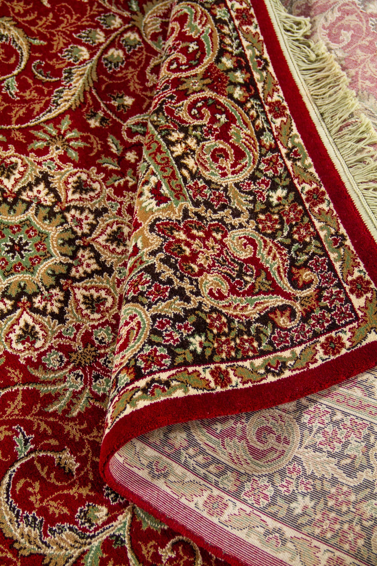 Detalle de alfombra roja doblada que deja ver el reverso tejido y el elaborado patrón floral de estilo oriental.