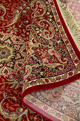 Detalle de alfombra roja doblada que deja ver el reverso tejido y el elaborado patrón floral de estilo oriental.
