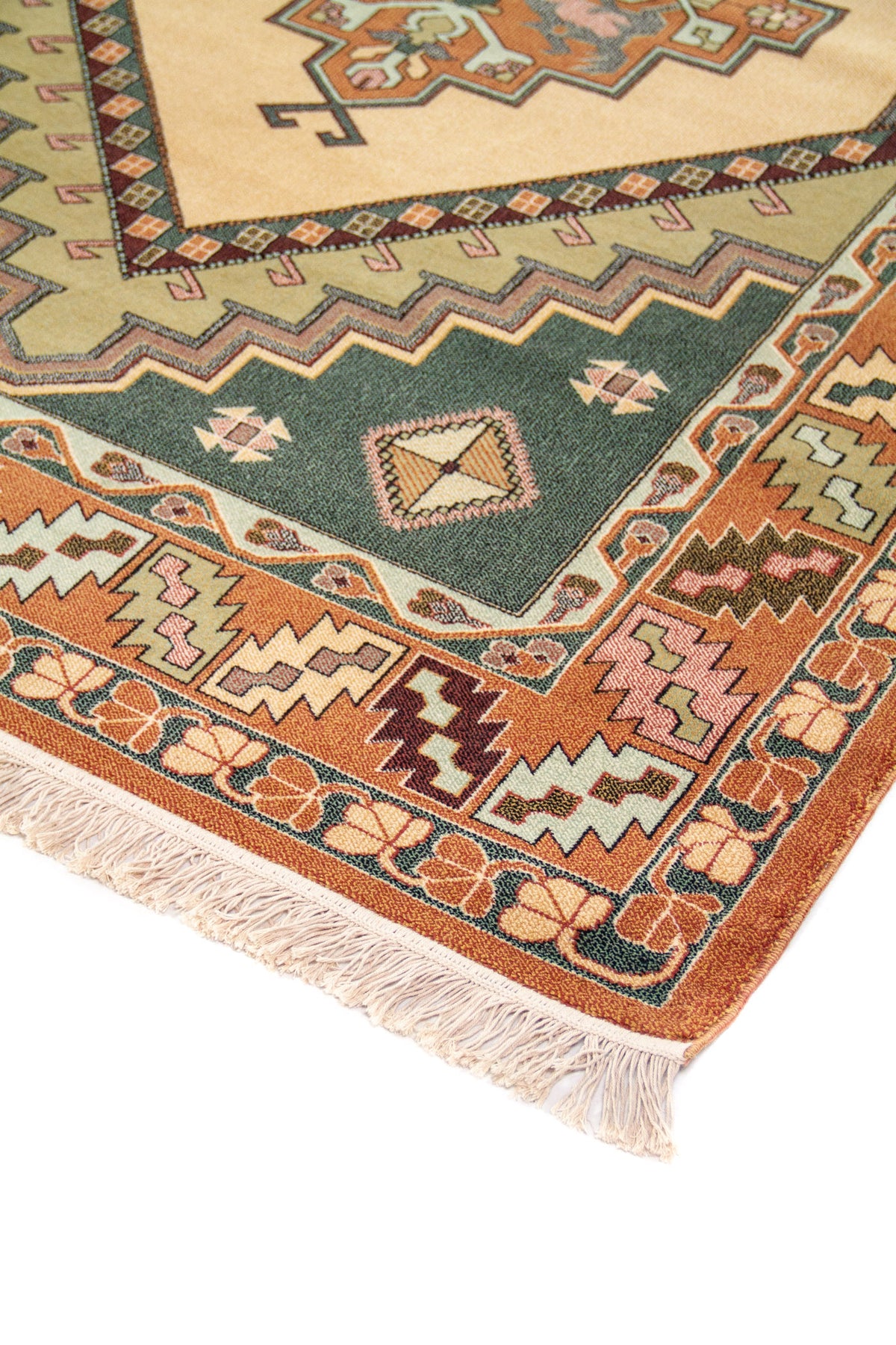 Detalle de esquina de alfombra con fondo beige, medallón geométrico, bordes en anaranjado oscuro y verde, y flecos claros