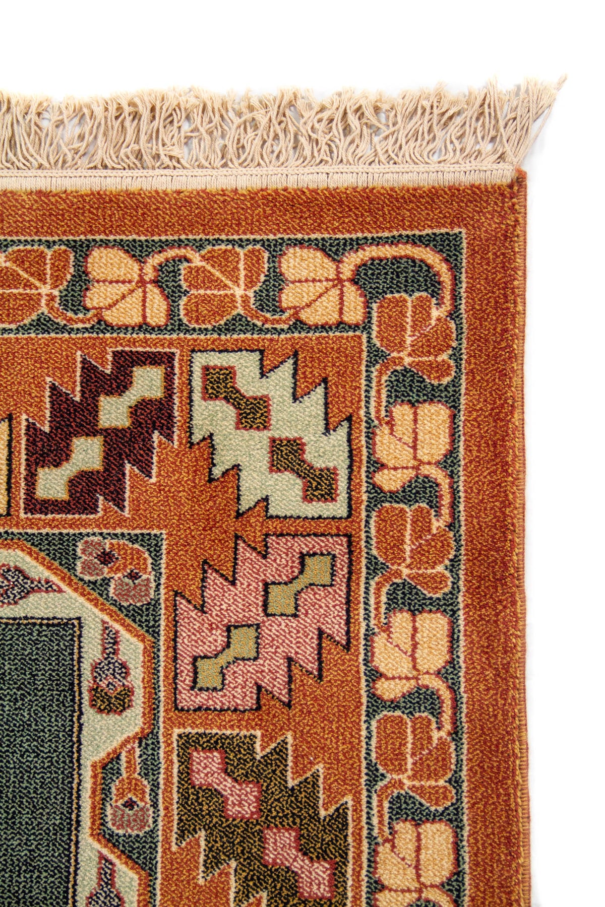 Detalle lateral de alfombra clásica con guarda geométrica en tonos anaranjado oscuro, verde, beige y marrón, y terminación con flecos