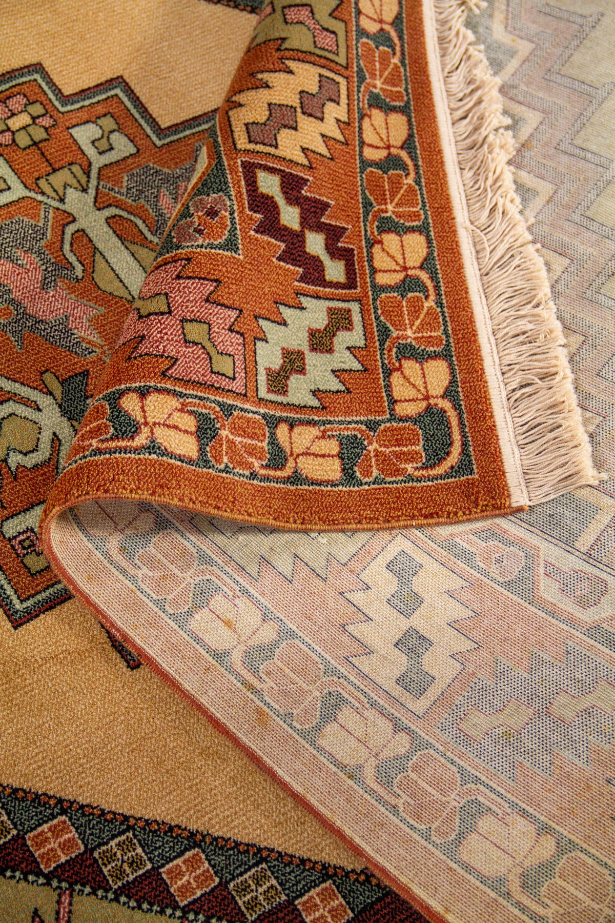 Detalle de alfombra doblada mostrando la textura, el reverso del tejido y el patrón geométrico del borde y del campo central