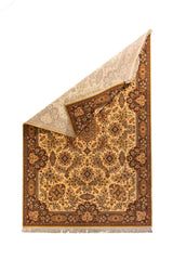 Alfombra beige de estilo clásico con una esquina doblada, mostrando el reverso del tejido y sus detalles florales ornamentales.