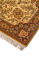 Detalle en perspectiva de esquina de alfombra clásica en tonos beige y rojo, con motivos florales densos, guarda oscura y flecos claros.