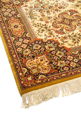 Primer plano de borde y esquina de alfombra ornamental en tonos beige, rojo y negro, con composición floral y acabado con flecos.