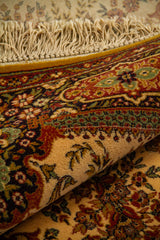 Alfombra doblada mostrando el reverso del tejido y un acercamiento a sus motivos florales en beige, rojo, verde suave y negro.