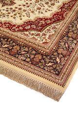 Detalle de esquina de alfombra oriental con flecos beige, guarda floral azul oscuro y patrones delicados en tonos blanco suave y rojo oscuro.