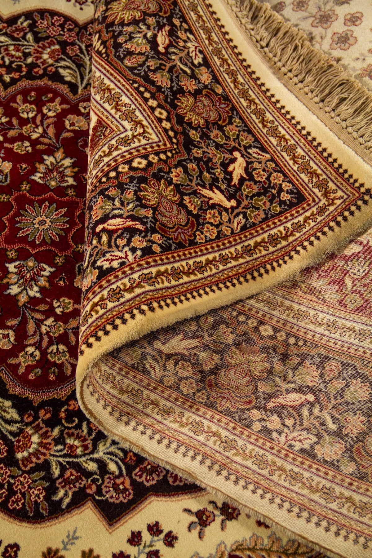 Detalle de alfombra doblada que deja ver el reverso tejido y el elaborado patrón floral de estilo clásico oriental.