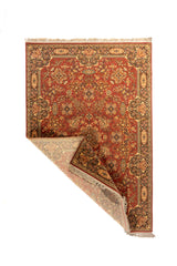 Alfombra oriental de estilo clásico con una esquina doblada que muestra el reverso, la estructura del tejido, la guarda decorativa y los flecos beige.