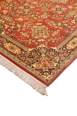Detalle en perspectiva de alfombra clásica en tono anaranjado oscuro con motivos florales finos, borde ornamental oscuro y flecos claros en el extremo.