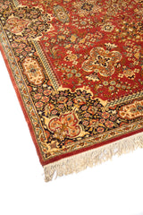 Acercamiento lateral de alfombra oriental con fondo anaranjado oscuro, diseño floral detallado y guarda decorativa en tonos beige, azul oscuro y verde.