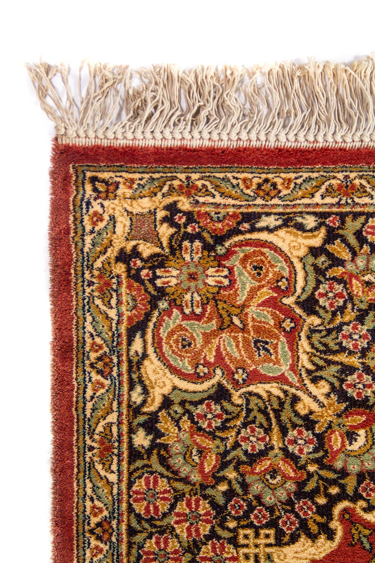 Primer plano de la esquina de una alfombra clásica con flecos beige, borde ornamental oscuro y motivos florales tradicionales.