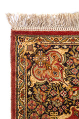 Primer plano de la esquina de una alfombra clásica con flecos beige, borde ornamental oscuro y motivos florales tradicionales.
