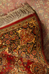 Detalle de alfombra oriental parcialmente doblada que deja ver el reverso, la textura del tejido y la riqueza del diseño floral del borde.