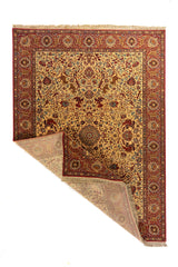 Alfombra clásica con esquina doblada que muestra el reverso, fondo beige, borde rojo y detallado diseño floral con motivos decorativos.