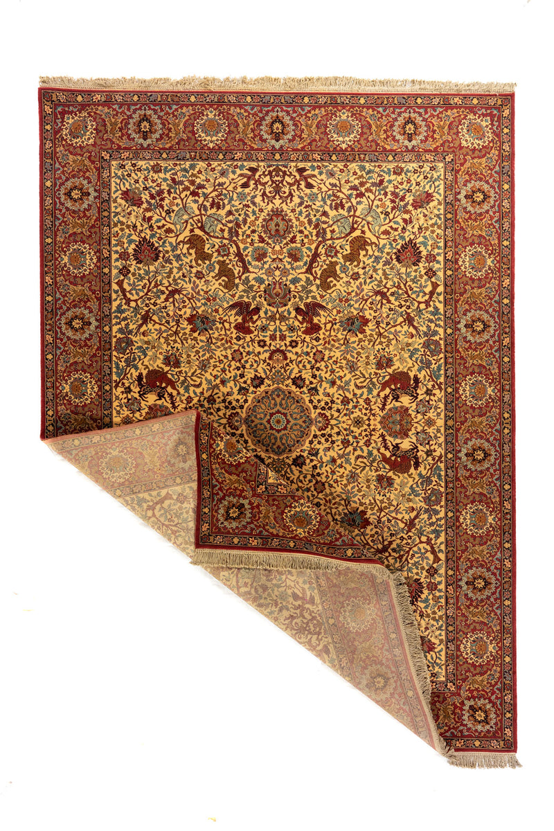 Alfombra clásica con esquina doblada que muestra el reverso, fondo beige, borde rojo y detallado diseño floral con motivos decorativos.