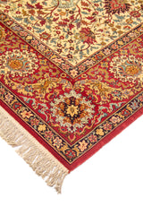 Detalle de esquina de alfombra con flecos beige, guarda roja y finos patrones florales en tonos azul, dorado y rojo.