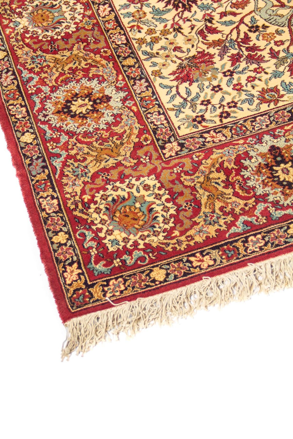 Primer plano de borde de alfombra oriental con fondo rojo, motivos florales ornamentales y acabado con flecos en tono beige.