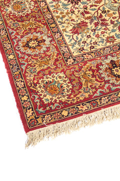 Primer plano de borde de alfombra oriental con fondo rojo, motivos florales ornamentales y acabado con flecos en tono beige.