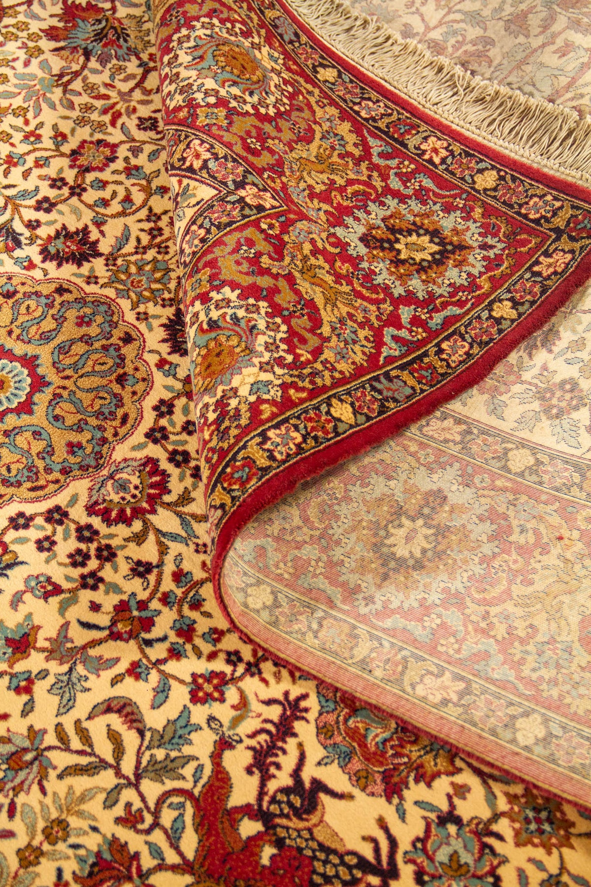Detalle de alfombra enrollada que muestra la textura, el reverso tejido y el diseño floral clásico en tonos beige, rojo y azul.