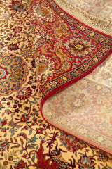 Detalle de alfombra enrollada que muestra la textura, el reverso tejido y el diseño floral clásico en tonos beige, rojo y azul.