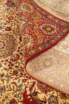 Detalle de alfombra enrollada que muestra la textura, el reverso tejido y el diseño floral clásico en tonos beige, rojo y azul.