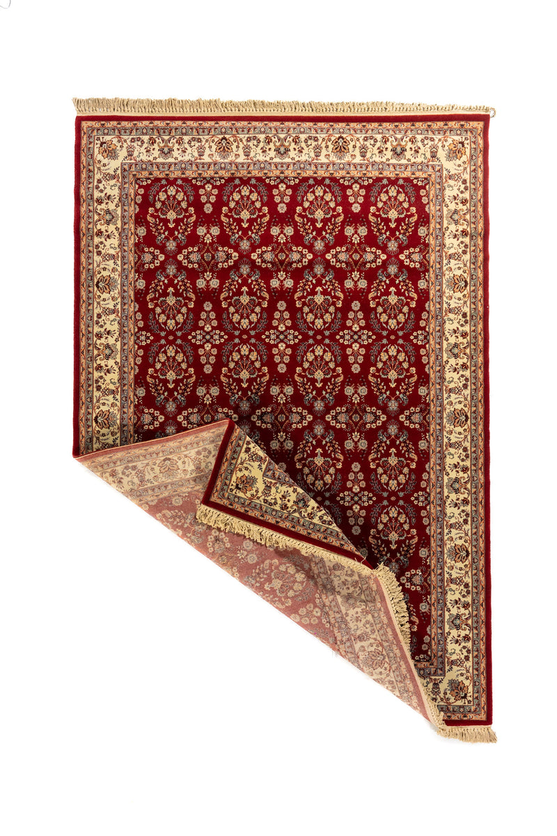 Alfombra roja con esquina doblada que muestra el reverso, patrones florales tradicionales, borde beige decorativo y flecos color beige.