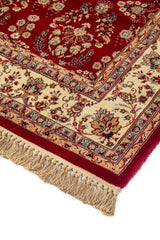 Primer plano del borde de una alfombra clásica roja con diseño floral, marco beige decorativo y acabado con flecos anudados