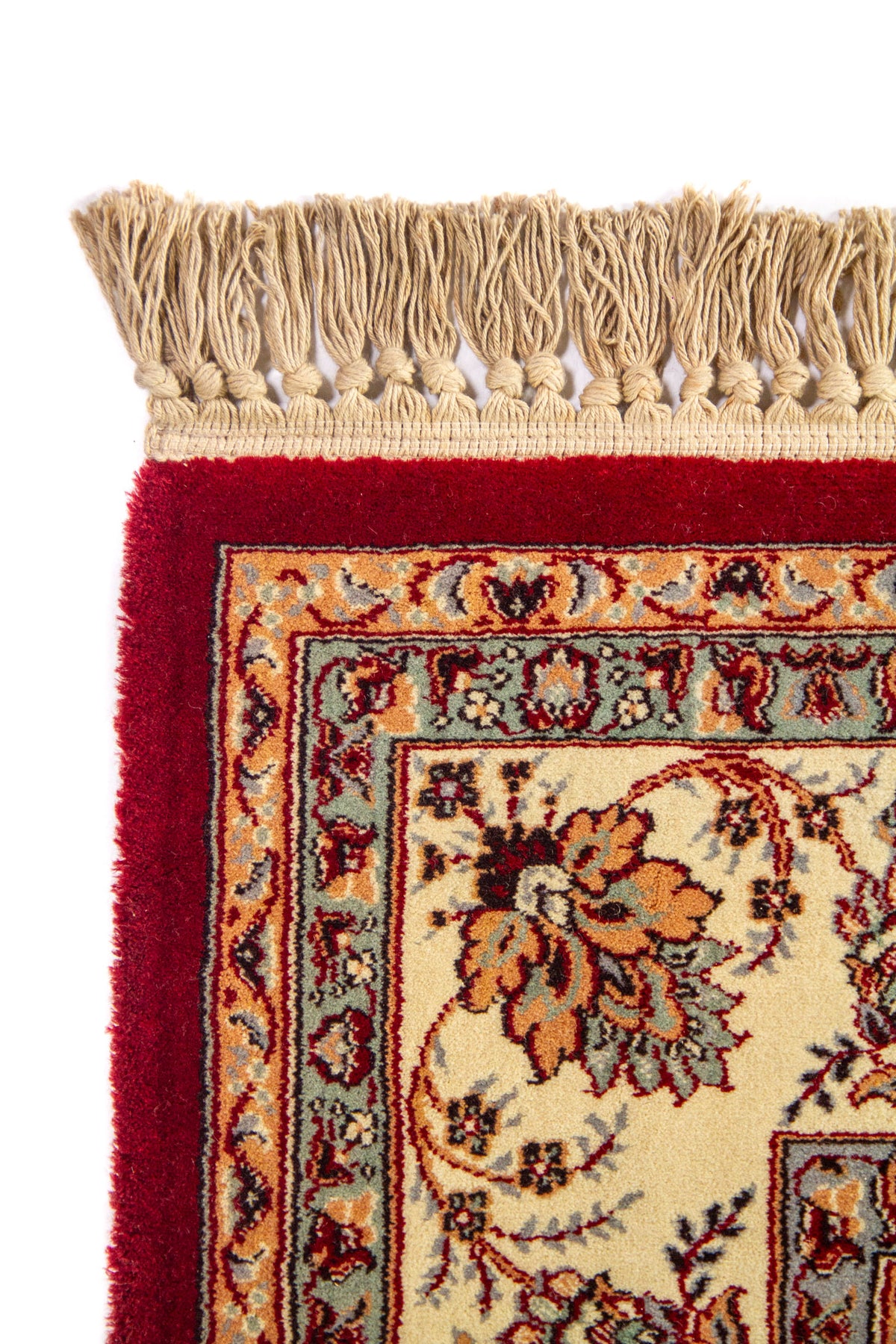 Detalle de esquina superior de alfombra roja con flecos beige, borde floral ornamentado y combinación de tonos blanco suave, azul suave y dorado.
