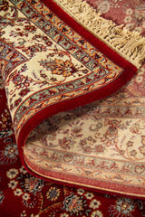 Alfombra parcialmente enrollada que muestra la textura, el reverso tejido y el diseño floral tradicional en rojo, beige y tonos suaves.