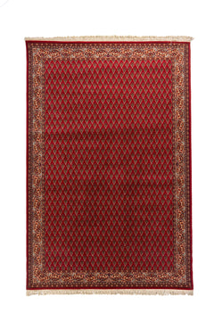 Alfombra oriental rectangular de fondo rojo intenso con guarda decorativa en tonos blanco suave, azul y rojo, y flecos claros en los extremos.